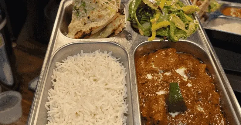 Indian Lunch Specials at Delhi Belly in Alhambra 1 Indian restaurant thali with butter chicken, steamed basmati rice, garlic naan, and mixed salad served on a stainless steel tray.