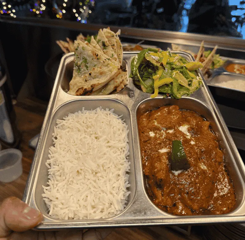 Indian restaurant thali with butter chicken, steamed basmati rice, garlic naan, and mixed salad served on a stainless steel tray.