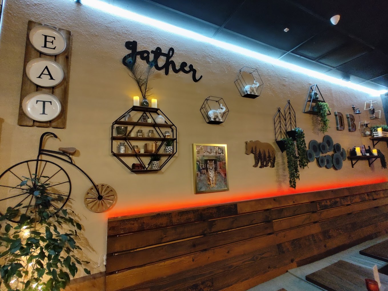 Indian Restaurant Cozy Wall Decor with Rustic and Vintage Art Indian restaurant cozy dining wall decor featuring rustic shelves, vintage bicycle art, plants, and "Gather" and "Eat" signs.